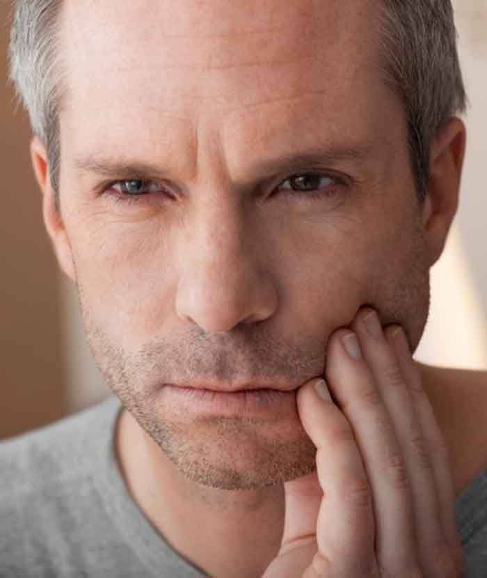 a man touching his cheek due to tooth pain